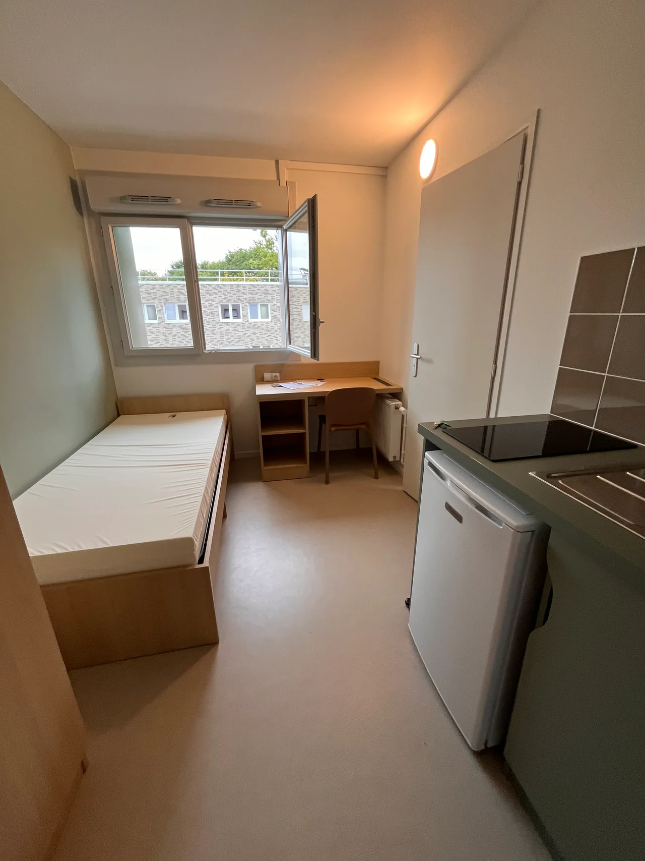 Bureau et lit dans une studette du bâtiment J, avec fenêtre ouverte