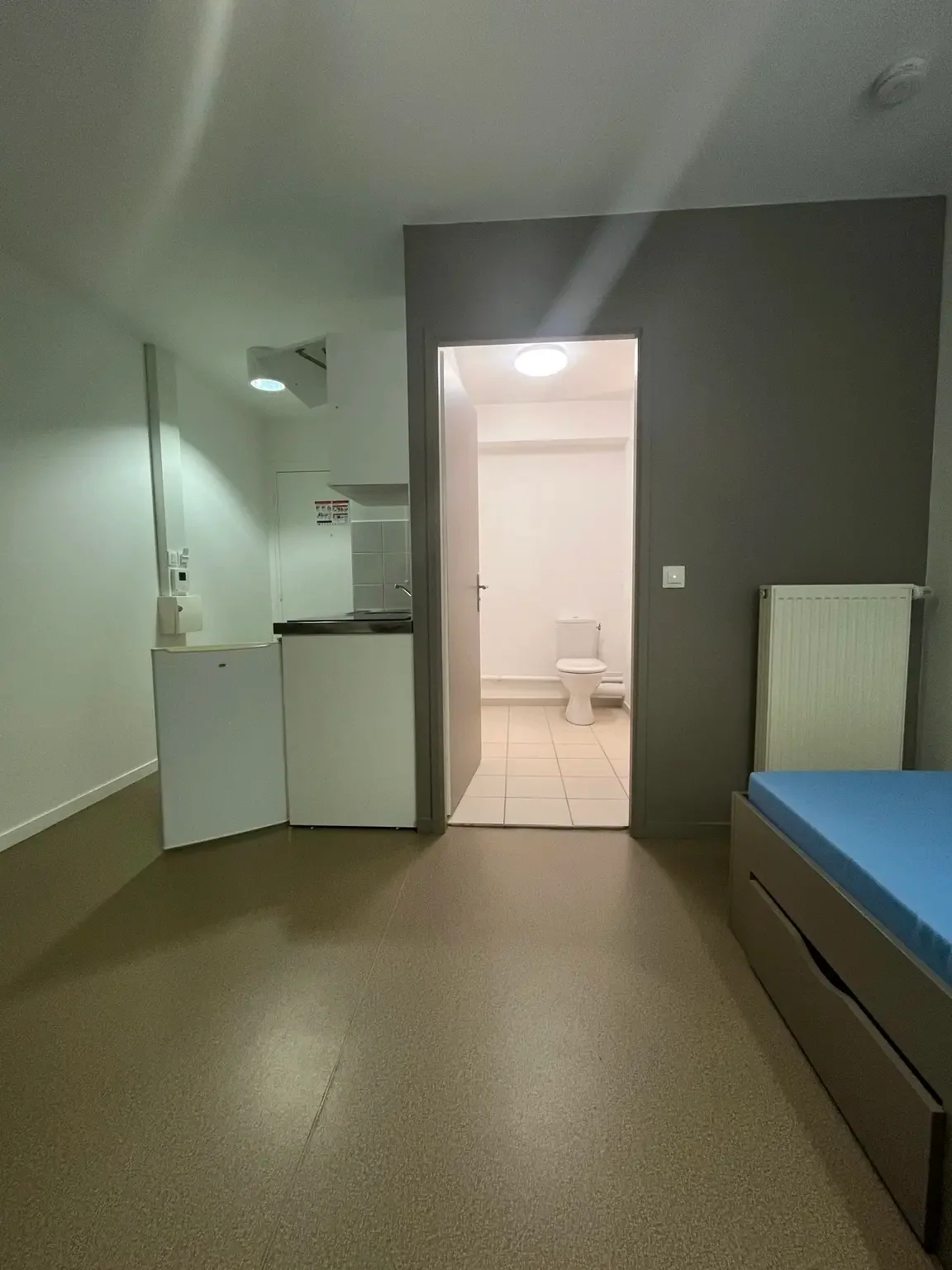 Vue d’ensemble d’un studio étudiant vide avec le lit, la kitchenette et la salle de bain